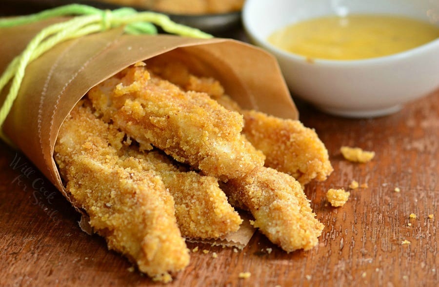 Chicken Fries wrapped up in butcher paper with a green string around them with a side of honey mustard in a small white bowl 