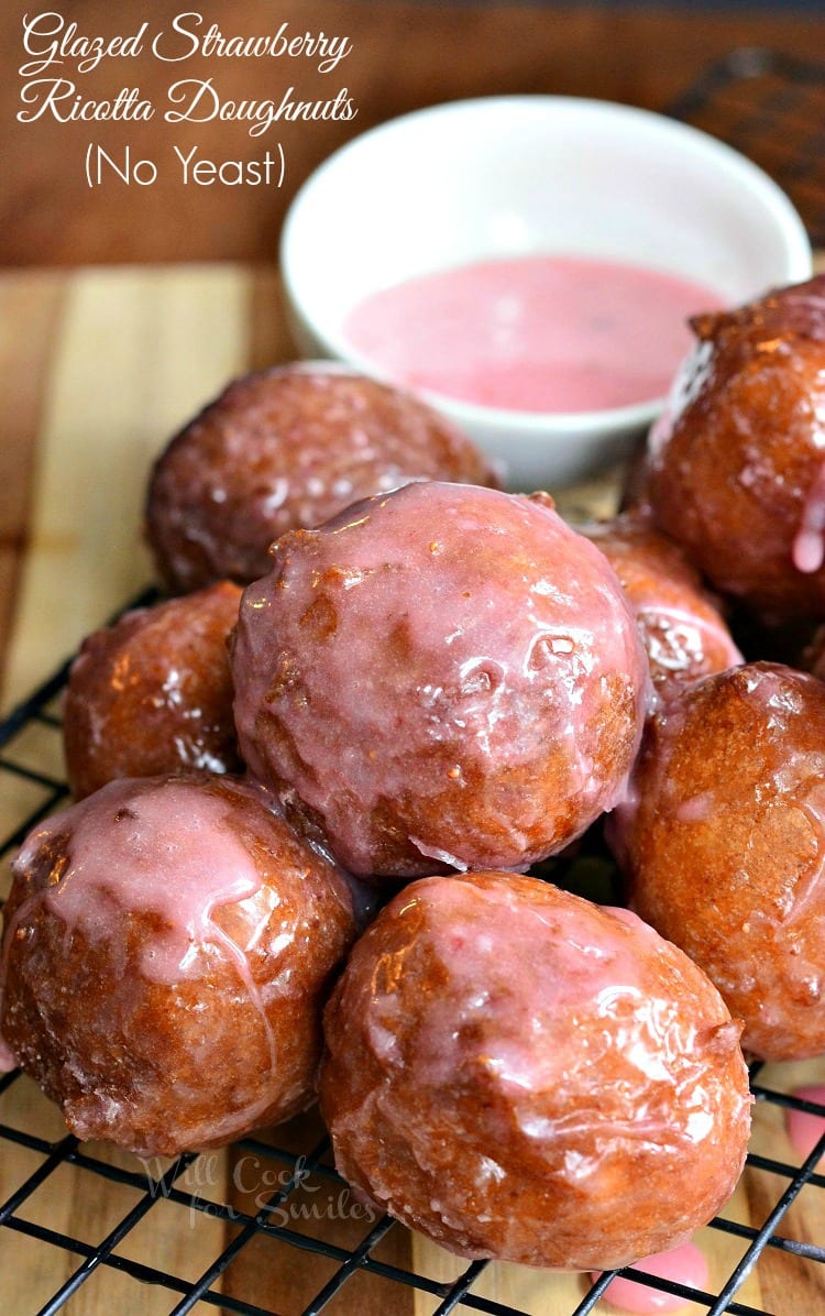 pile of strawberry glazed doughnuts on a wire cooling rack with a small white dish and dipping sauce in the background
