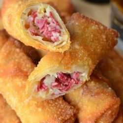 White saucer in foreground with dipping sauce in front of stacked egg rolls and a bottle of red irish beer as viewed from close up and above