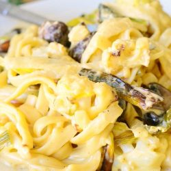 Small white decorative plate filled with roasted cauliflower and mushroom fettuccine in garlic cheese sauce with a fork on the plate in the background