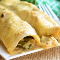 Roasted pablano and chicken enchiladas on a white rectangular plate with a green and white cloth in the background and a fork to the right viewed close up