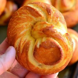 siracha honey pretzel knots on a baking tray with a hand holding one above the rest