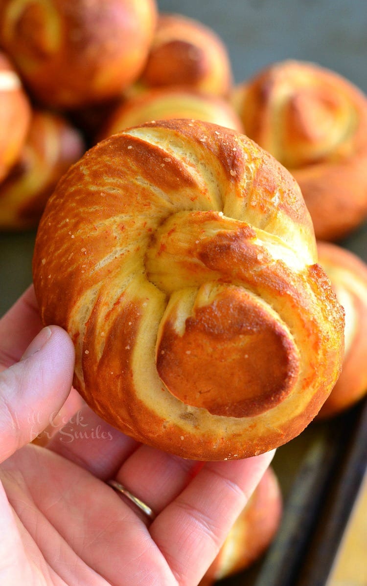 siracha honey pretzel knots on a baking tray with a hand holding one above the rest