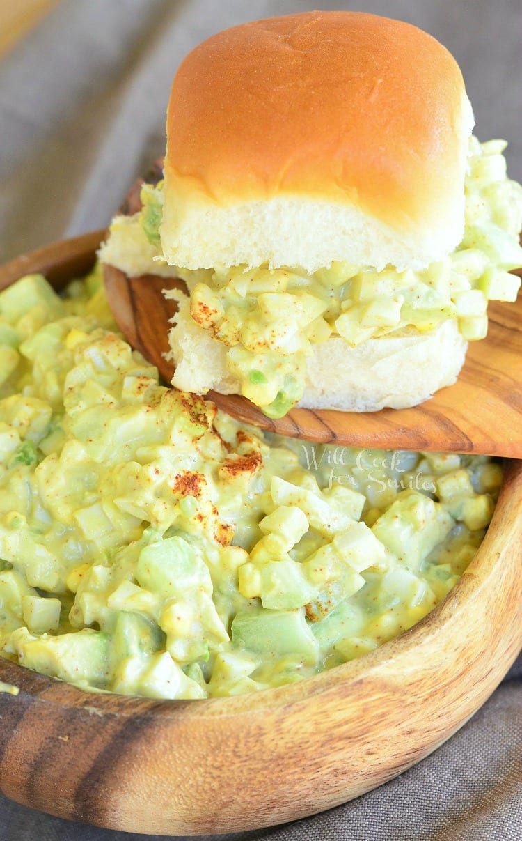 Avocado Cucumber Egg Salad in a wood bowl with a wood spoon and a egg salad sandwich on top of the wooden spoon 