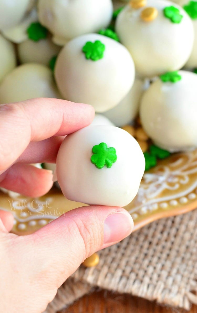 holding a Bailey's Cookie Dough Truffles with shamrock candy on top in my hand and the rest on a yellow plate 