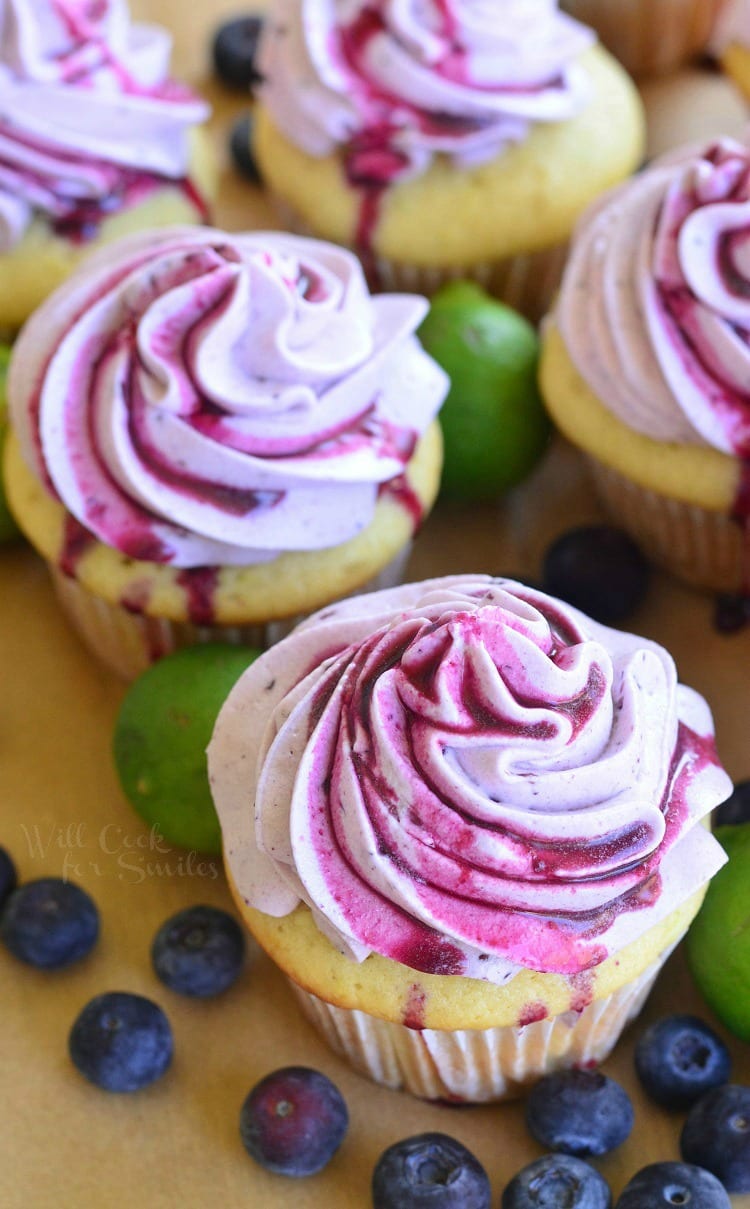 Top view of Cupcakes with Fresh Blueberry Cream Cheese Frosting on a cutting board with blueberries and limes 