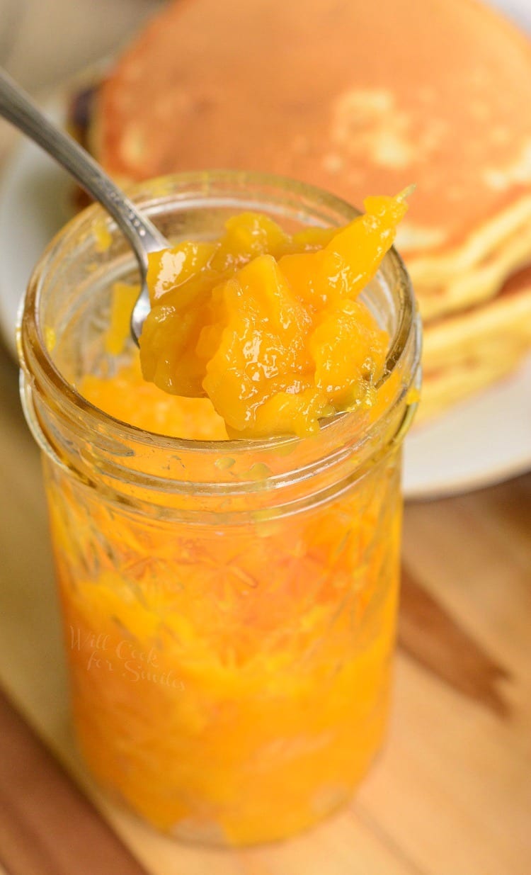 Mango jam in a glass jar with pancakes in the background 