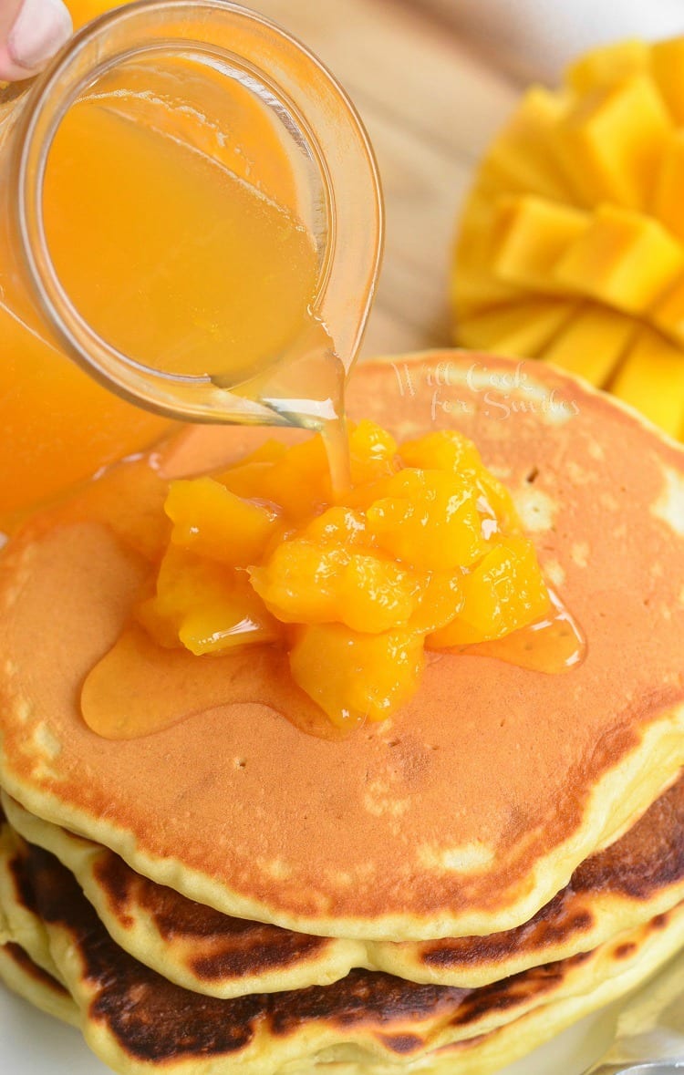 pouring Mango Syrup over pancakes that have mangos on top 