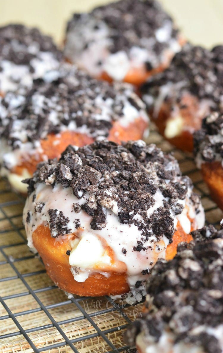 Oreo Cheesecake Doughnuts with crushed oreas on top on a cooling rack 