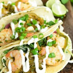 tequila lime shrimp tacos with sour cream drizzled on top on a cutting board