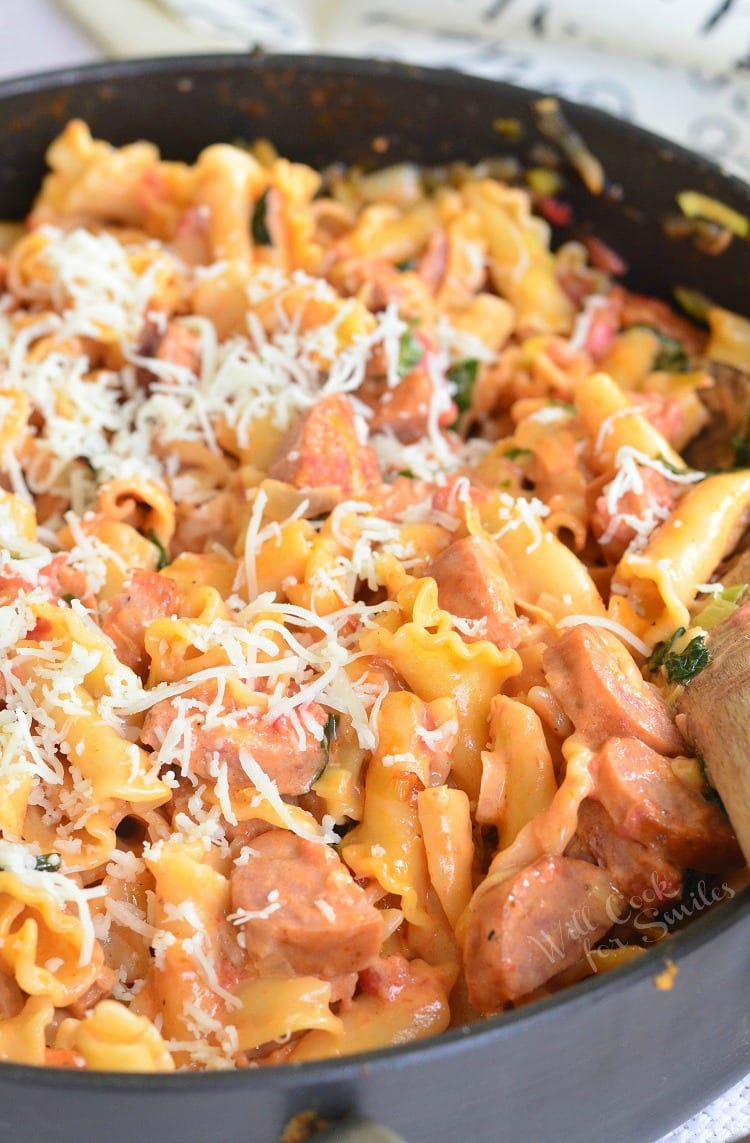 Tomato Basil Sausage and Pasta Skillet with cheese on top in a pan with a wooden spoon 
