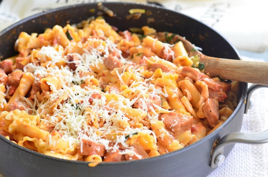 Tomato Basil Sausage and Pasta Skillet with cheese on top in a pan with a wooden spoon 