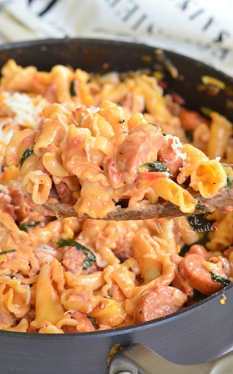 Tomato Basil Sausage and Pasta Skillet with cheese on top in a pan with some on a wooden spoon 