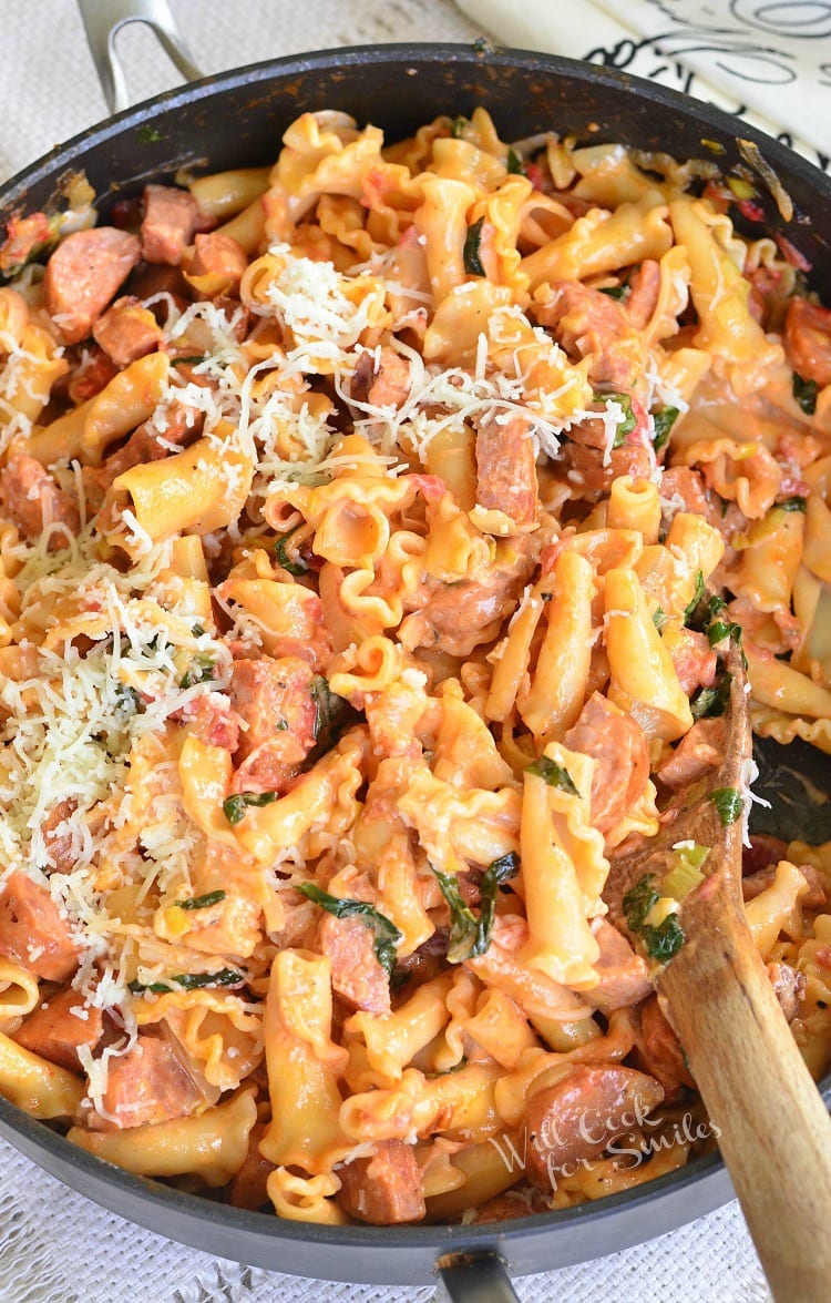 Tomato Basil Sausage and Pasta Skillet with cheese on top in a pan with a wooden spoon 