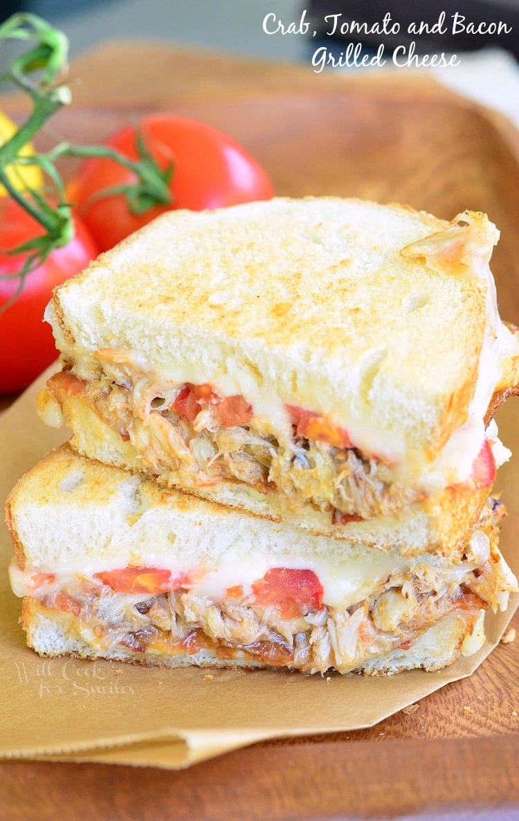 Tomato, Bacon and Crab Grilled Cheese cut in half on parchment paper with tomatoes in the background  