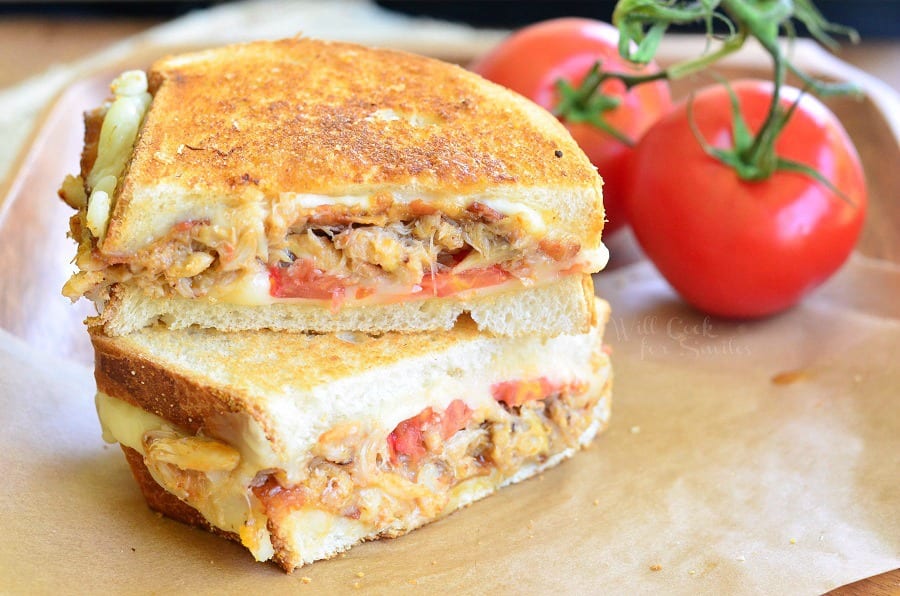 Tomato, Bacon and Crab Grilled Cheese cut in half on parchment paper with tomatoes in the background  