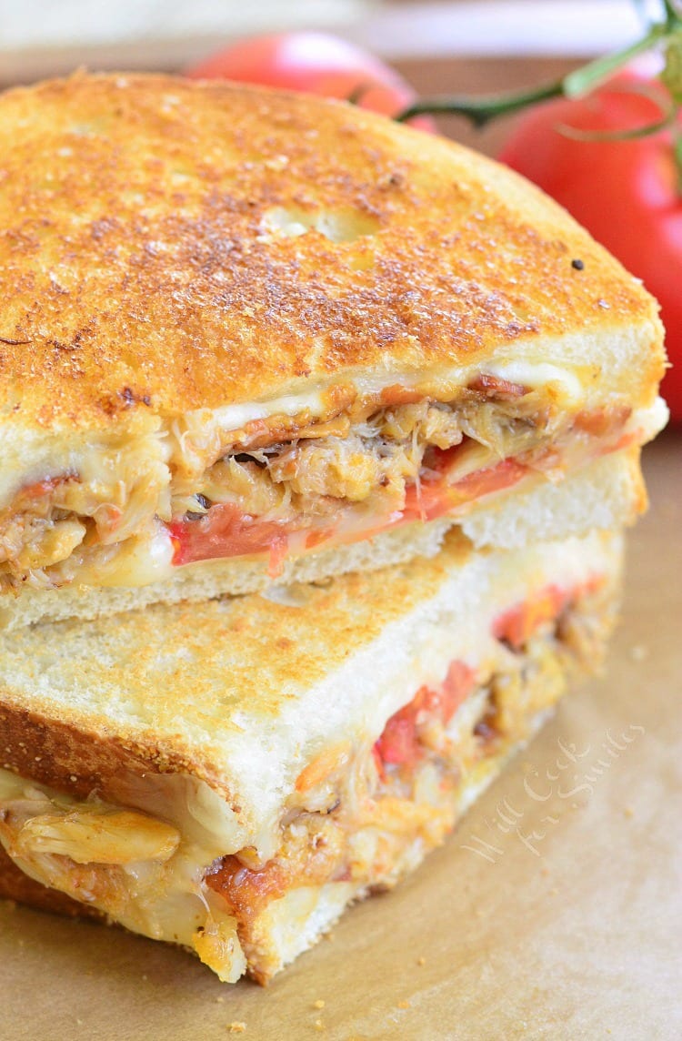 Tomato, Bacon and Crab Grilled Cheese cut in half on parchment paper with tomatoes in the background  