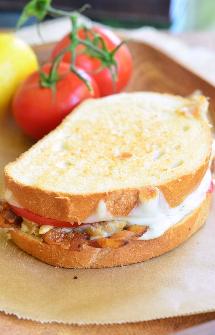 Tomato, Bacon and Crab Grilled Cheese on parchment paper with tomatoes in the background  