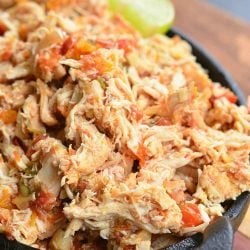 Black skillet filled with crock pot shredded salsa chicken on a wooden cutting board with a lime garnish along the side of the skillet