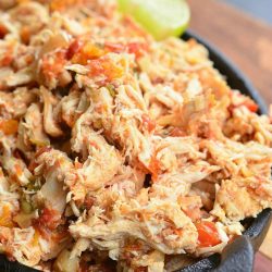 Black skillet filled with crock pot shredded salsa chicken on a wooden cutting board with a lime garnish along the side of the skillet