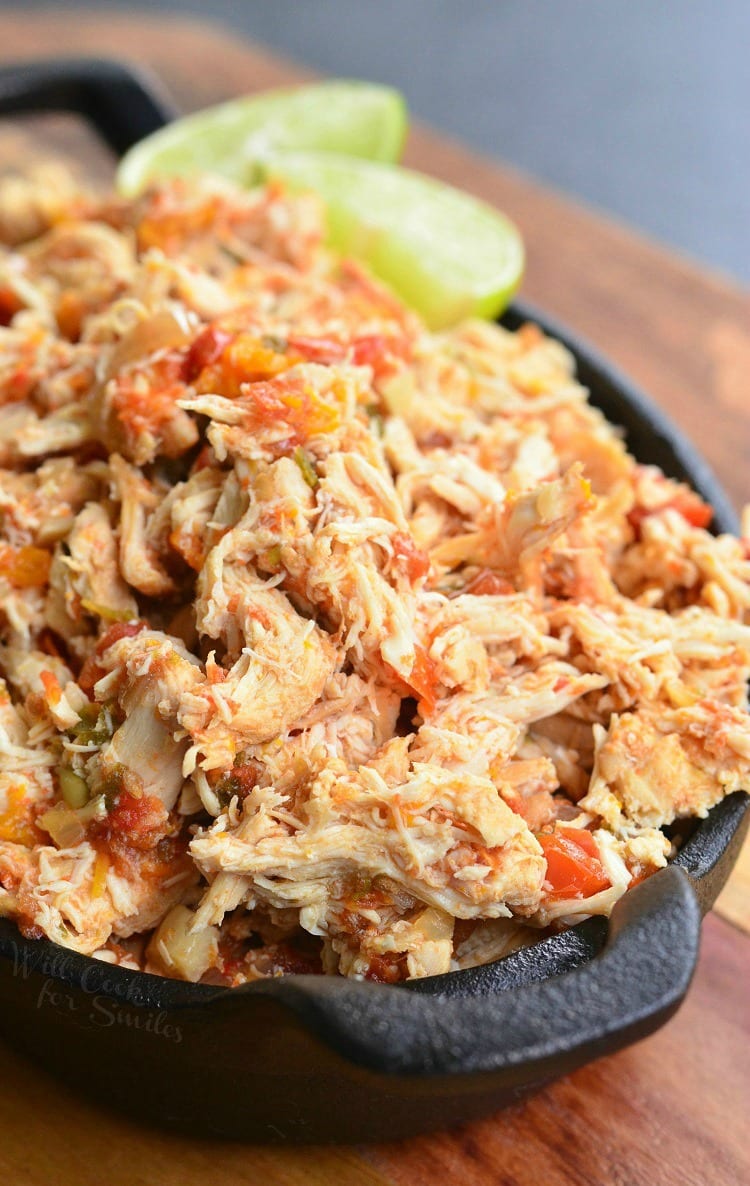 Black skillet filled with crock pot shredded salsa chicken on a wooden cutting board with a lime garnish along the side of the skillet