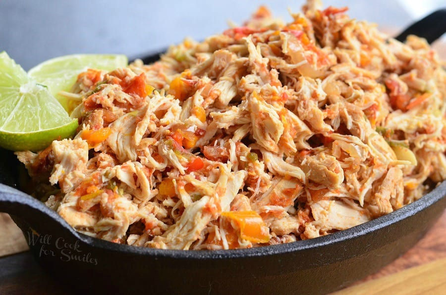 Close up view of crock pot shredded salsa chicken on a black skillet with a lime garnish on a wooden cutting board
