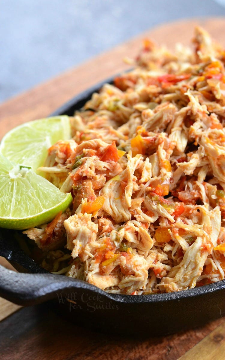 Close up view of crock pot shredded salsa chicken on a black skillet with a lime garnish on a wooden cutting board viewed at a slight angle