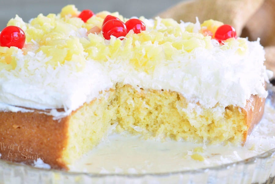 Tres Leches Cake with a slice missing white coconut frosting, pineapple and cherries on top 