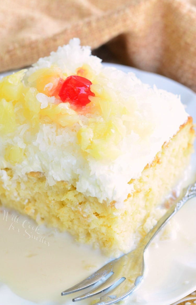 a slice of Tres Leches Cake with white coconut frosting, pineapple and a cherry on top 