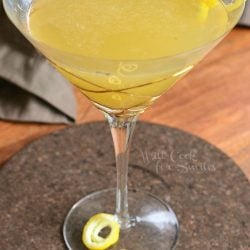 Decorative martini glass filled with pineapple lemon martini with lemon peel garnishes on the rimand around the stem of the glass as viewed from above