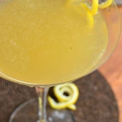 Decorative martini glass filled with pineapple lemon martini with lemon peel garnishes on the rimand around the stem of the glass as viewed close up and from above