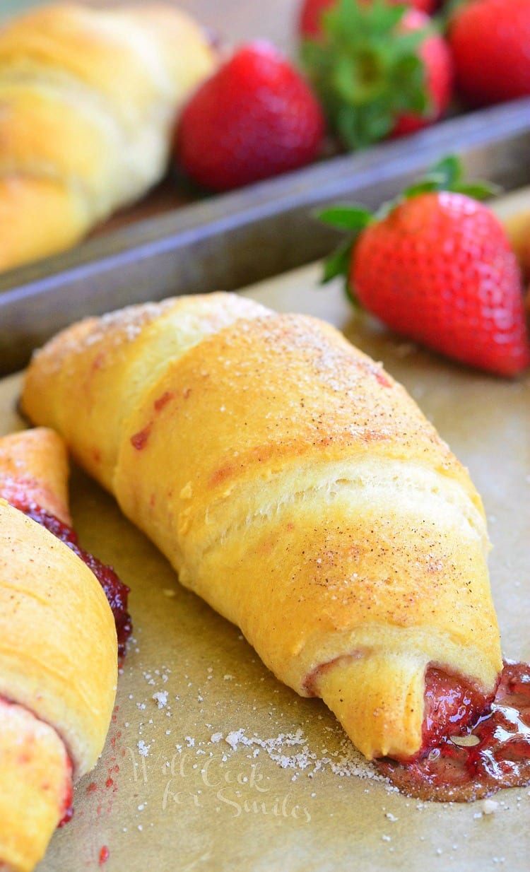 crescent rolls with strawberry jam inside them on a baking shit with parchment paper and strawberries in the background