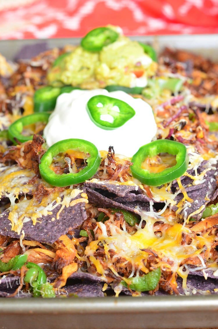 Pulled Pork Nachos on a baking sheet with sour cream on top and slices of jalapeno and guacamole 