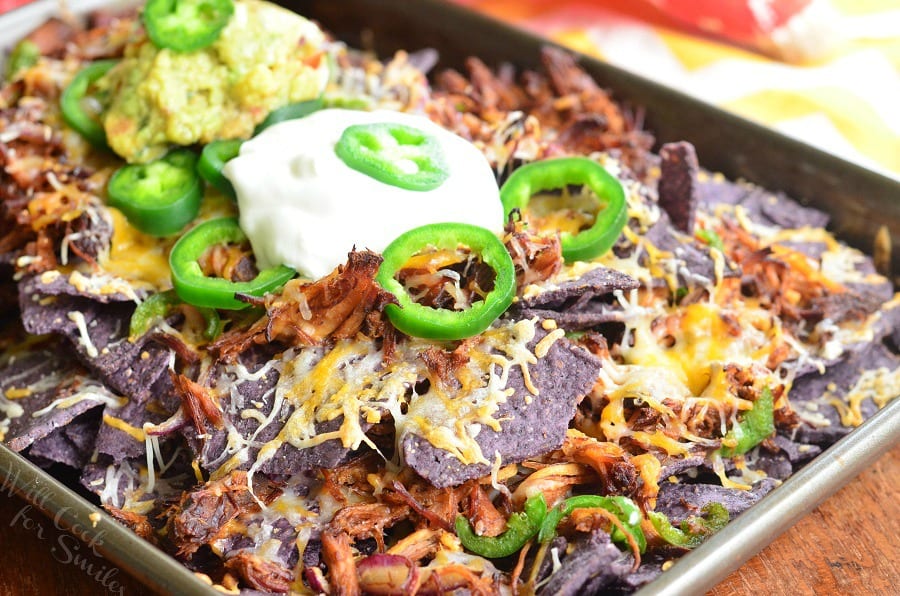 Pulled Pork Nachos on a baking sheet with sour cream on top and slices of jalapeno and guacamole 