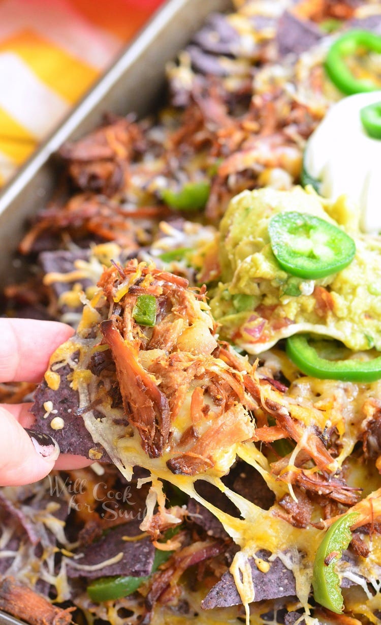 picking up a Pulled Pork Nachos on a baking sheet with slices of jalapeno and guacamole 