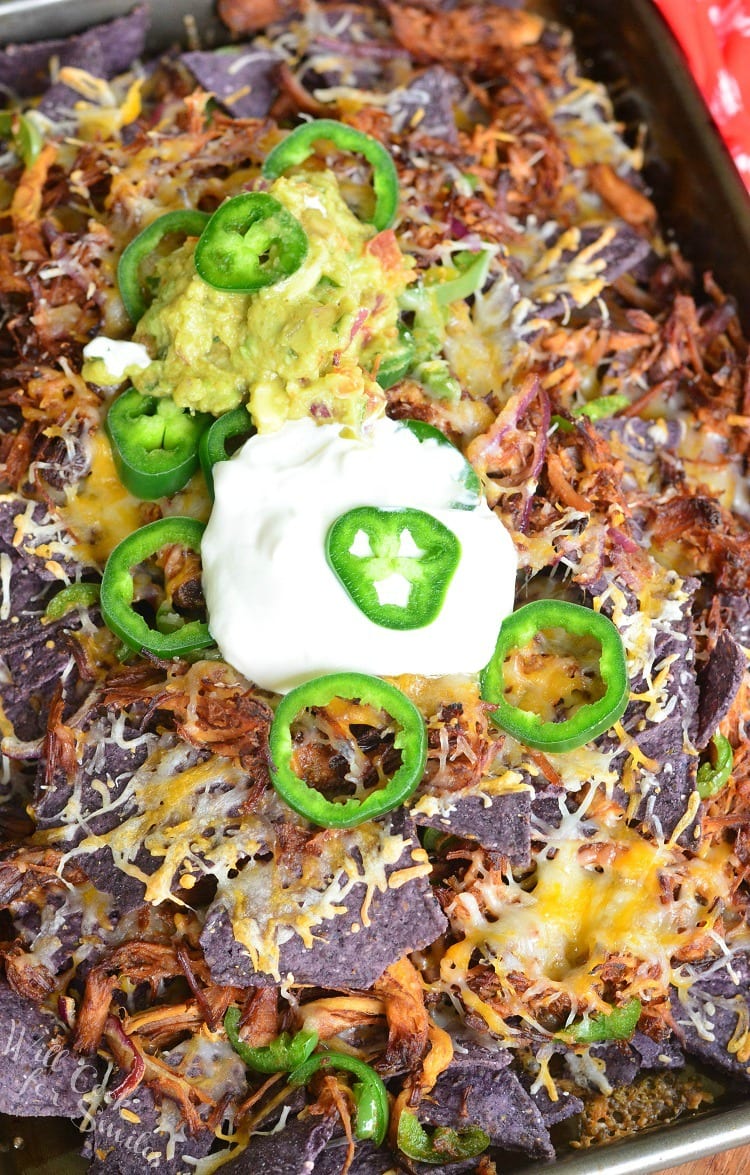 Pulled Pork Nachos on a baking sheet with sour cream on top and slices of jalapeno and guacamole 