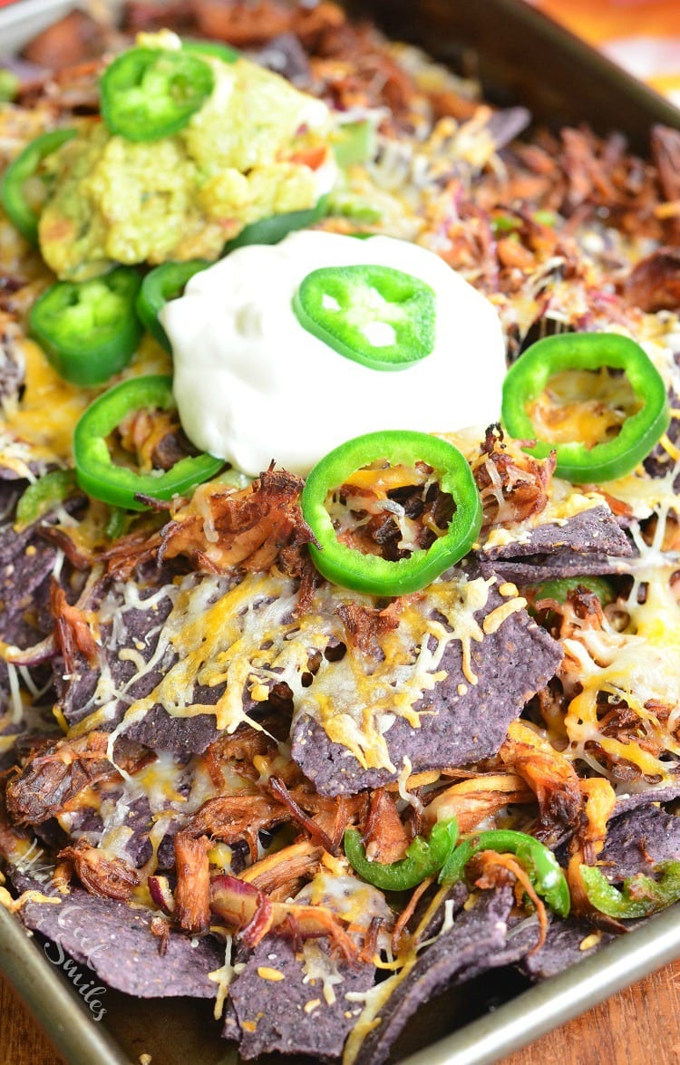 Pulled Pork Nachos on a baking sheet with sour cream on top and slices of jalapeno and guacamole 