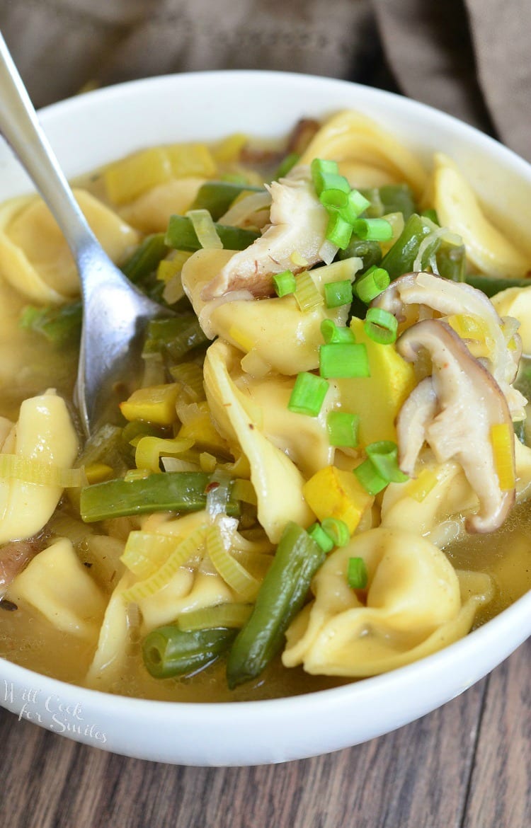 Vegetable Medley Tortellini Soup in a white bowl with green onion as garnish and a spoon sitting in it 