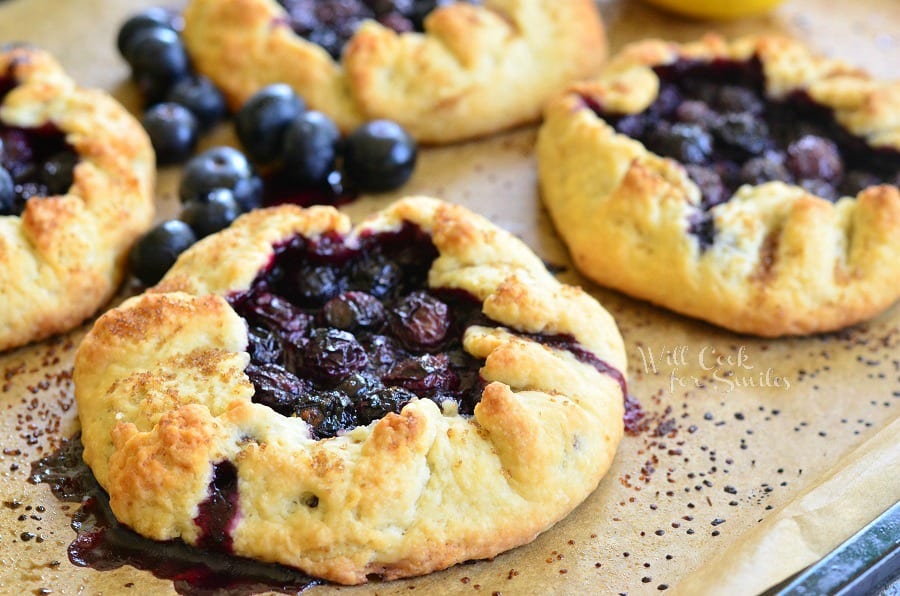 horizontal image of Blueberry Vanilla Lemon Galette on parchment paper with blueberries around it 