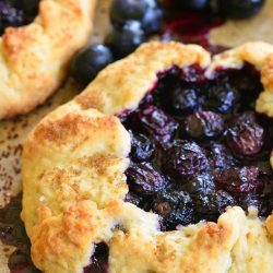 several lemon blueberry galettes on wax paper on a metal baking sheet tray with blueberries scattered between as viewed from above and close up