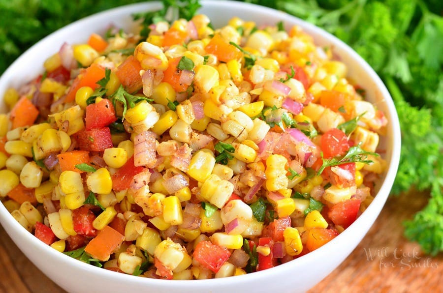 horizonal photo of Cajun Corn Salad with corn, red and orange bell peppers, red onion, an cilantro in a white bowl