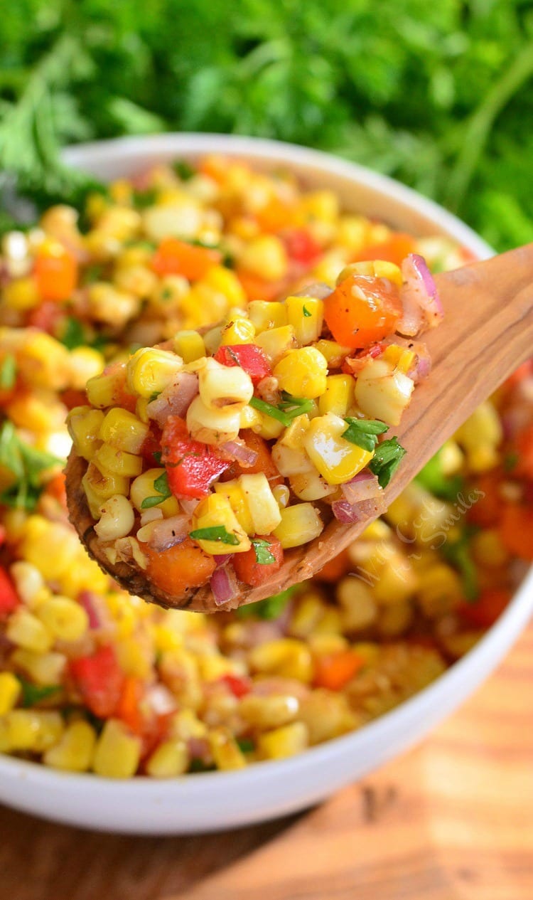 Cajun Corn Salad with corn, red and orange bell peppers, red onion, on a a wooden spoon with the bowl in the background 
