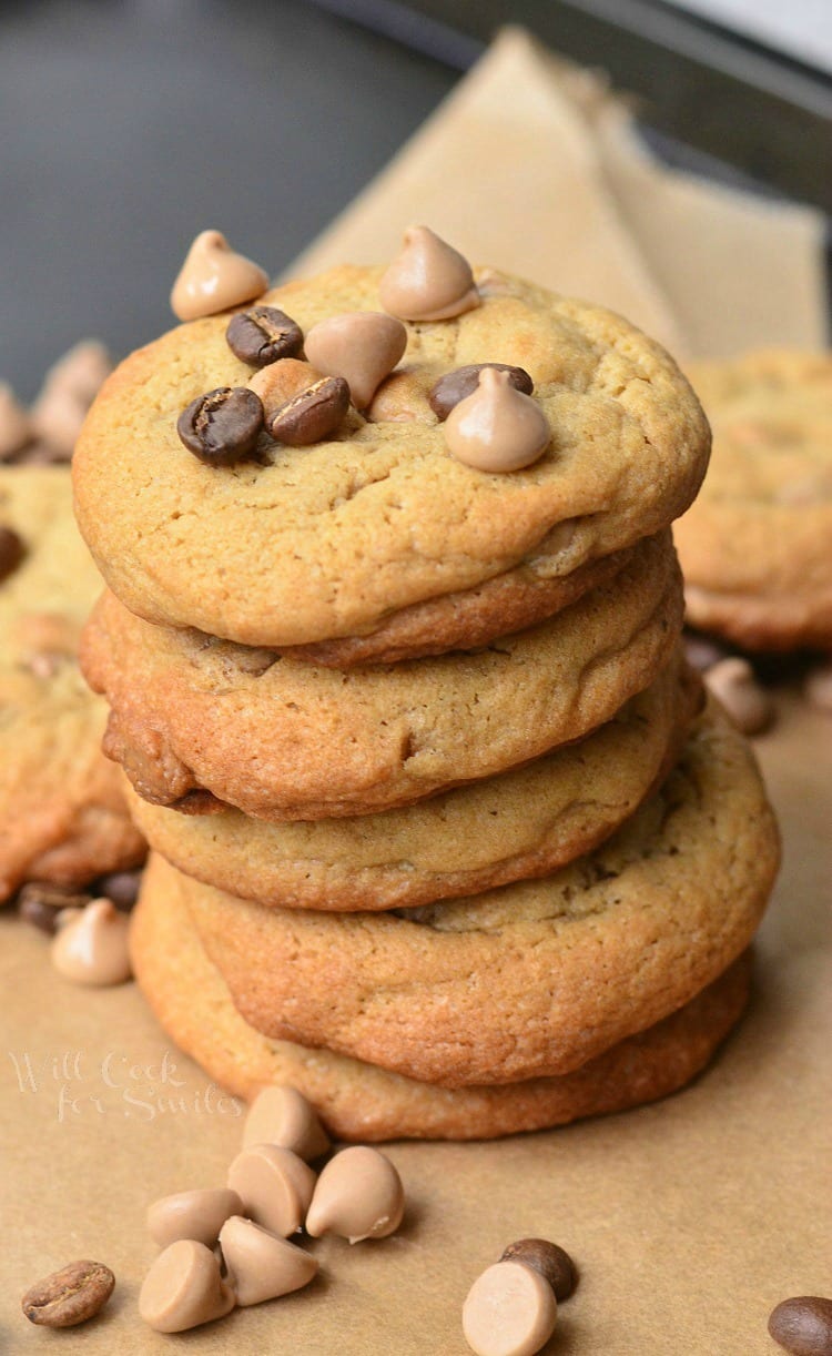 Cappuccino Cookies stacked up on parchment paper with chocolate chips and cappuccino chips around it and on top 
