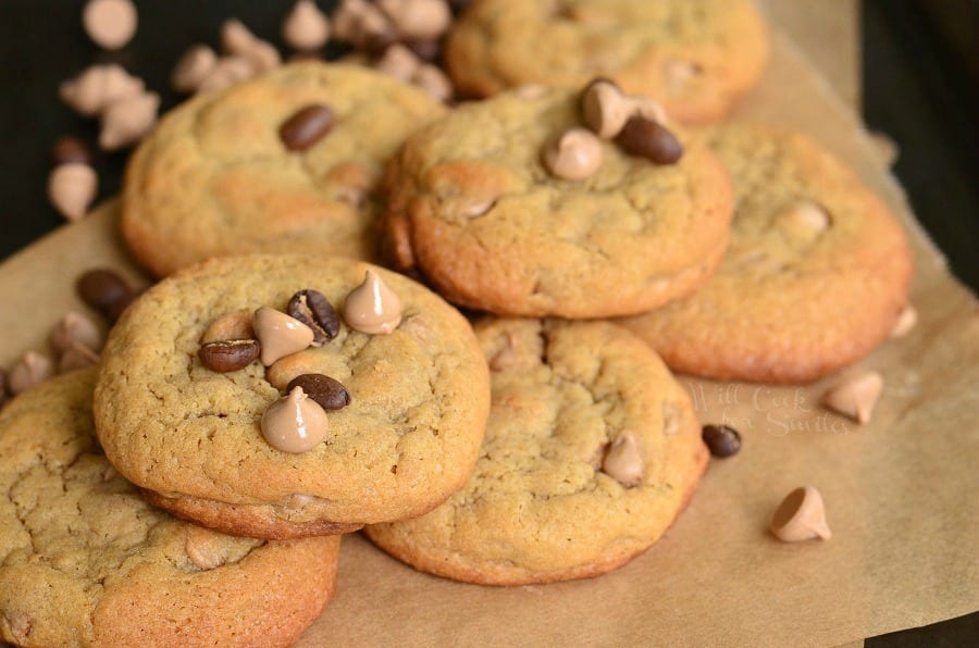 Cappuccino Cookies stacked up on parchment paper with chocolate chips and cappuccino chips around it and on top 