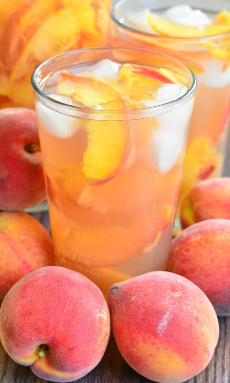 Ginger Peach and Honey Iced Green Tea in a glass with ice and peaches surrounded by peaches on a wood table 