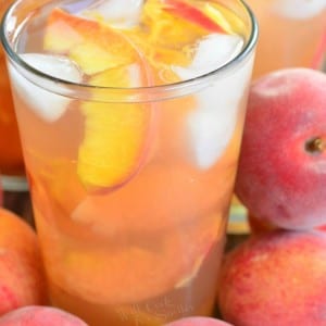 glasses full of peach iced tea with peach slices and ice with more peaches around.