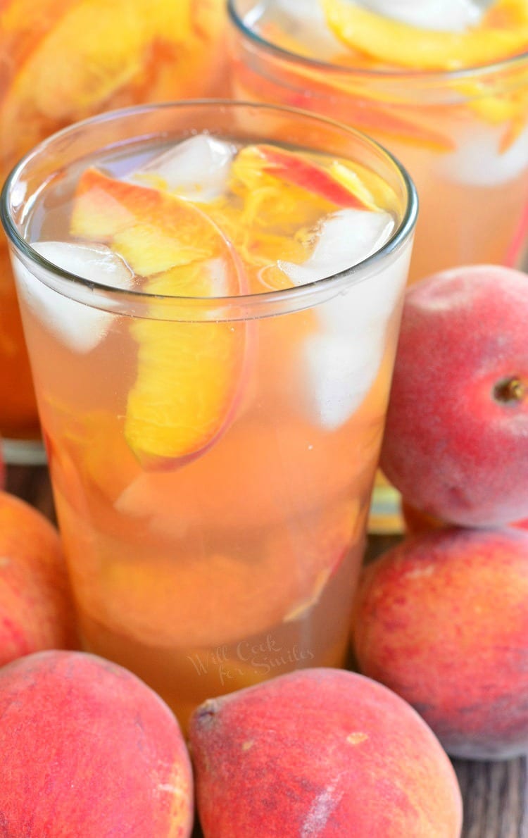 glasses full of peach iced tea with peach slices and ice with more peaches around.