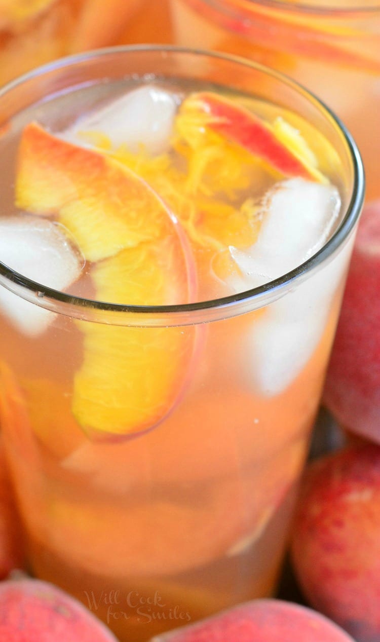 Ginger Peach and Honey Iced Green Tea in a glass with sliced peaches and ice on a table with peaches around it 