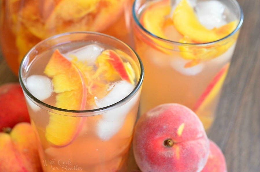 Ginger Peach and Honey Iced Green Tea in a glass with sliced peaches and ice on a table with peaches around it 