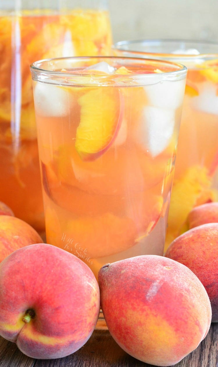 glass with iced green tea and sliced peaches with whole peaches around the glass.